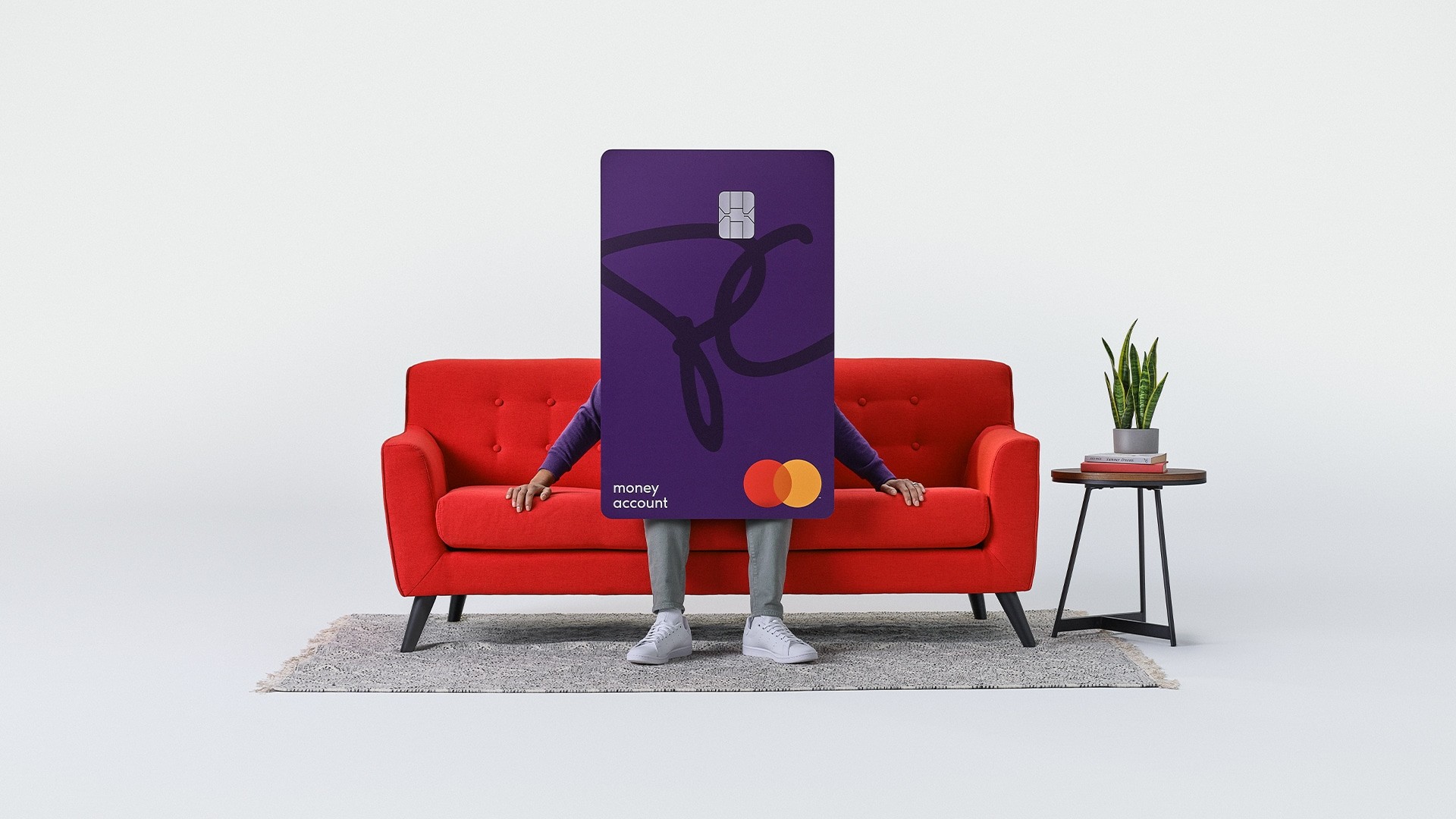 A human-sized PC Money Account card sits on a couch.