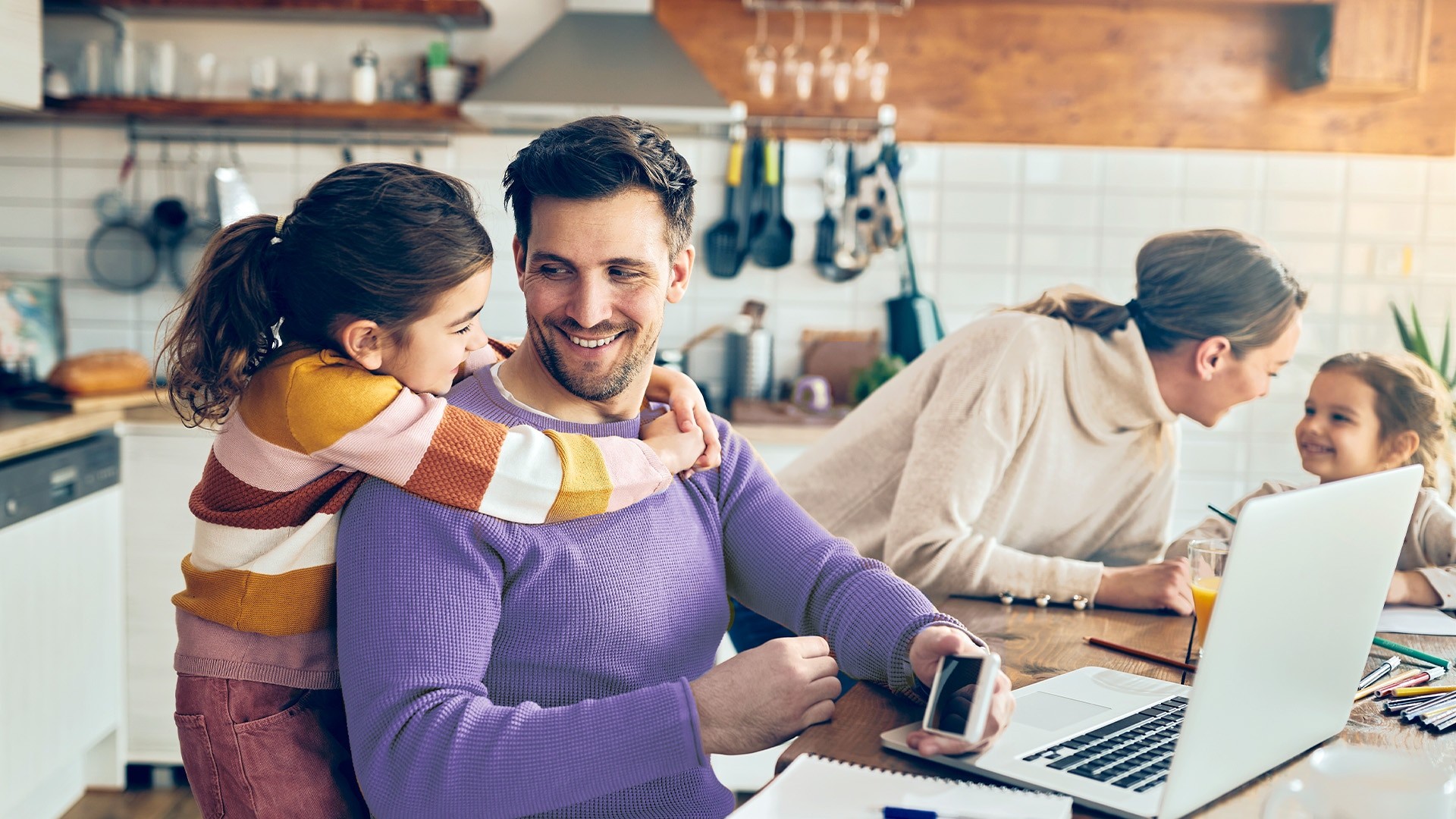 Two parents with young kids working on a laptop in the kitchen.