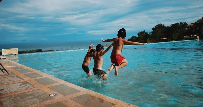 3 kids jumping into a large swimming pool